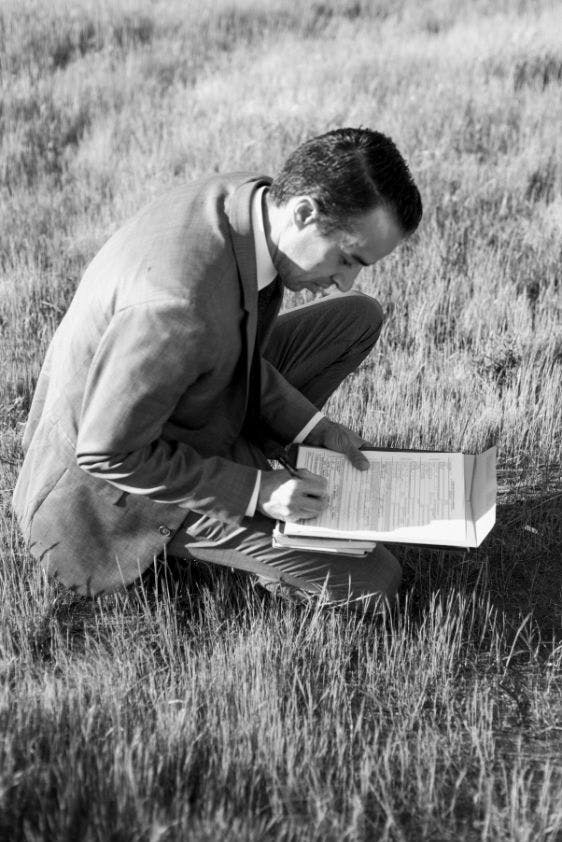 a black and white photo of jacob signing a marriage license while he is kneeling down on the grass