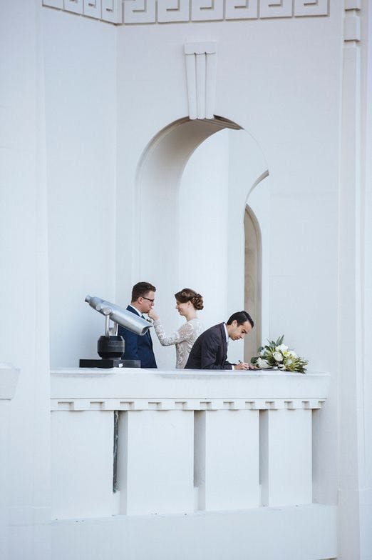 a photo of jacob signing a marriage license under the arches of Griffith Observatory with the couple having a moment behind him.