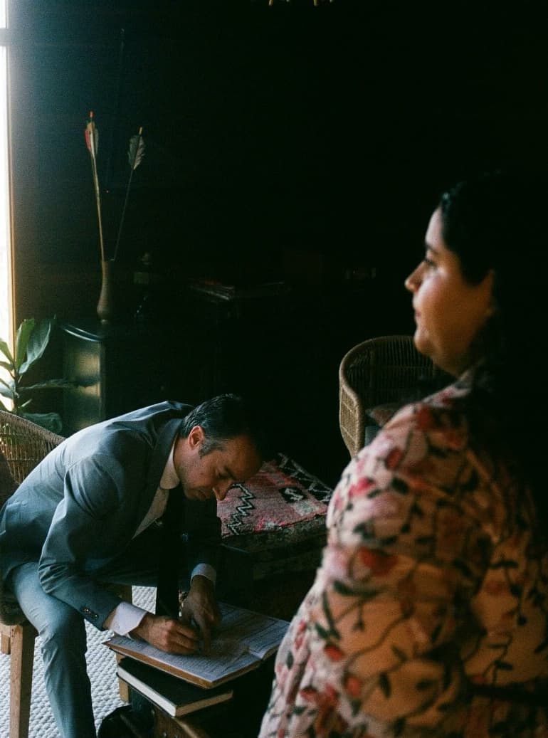 jacob signing the marriage license at the table as the couple looks on